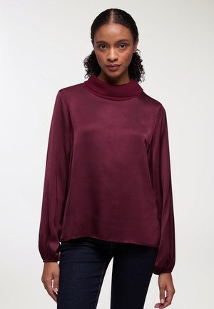 Blusa in satin borgogna con colletto alto, maniche lunghe a palloncino e vestibilità ampia. Tessuto liscio con una leggerissima lucentezza.