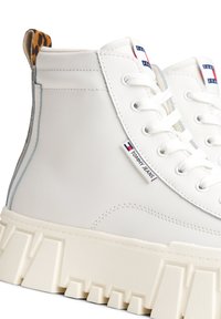 Baskets montantes blanches en simili cuir lisse, avec une semelle blanche épaisse, des lacets ronds et une touche d'imprimé léopard au niveau du talon.