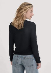 Schwarzes Langarmshirt mit rundem Ausschnitt, kombiniert mit hellblauen Jeans im entspannten Schnitt und mit Gesäßtaschen.