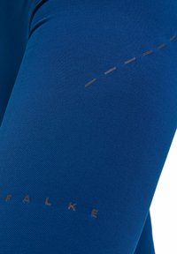 Leggings sportivi blu realizzati in tessuto testurizzato, con un logo sottile e linee tratteggiate per dettagli di design.