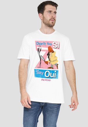White cotton T-shirt featuring a graphic print with vibrant colors and text: “Don’t Say SI” and “Say Oui” with a cartoon character design.
