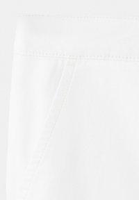 Gros plan sur un tissu blanc montrant des détails de couture diagonale et une couture, mettant en valeur la texture et la construction du vêtement.
