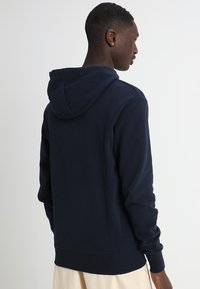 Sudadera con capucha de color azul marino, confeccionada en mezcla de algodón, con un bolsillo tipo canguro, puños acanalados y dobladillo, de textura suave y diseño casual.