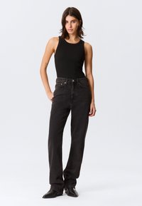 Top preto de alças e jeans pretos de cintura alta com corte reto. Tecido liso, detalhes mínimos, usado com botas pretas de cano curto.