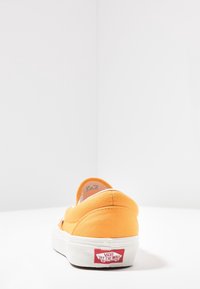 Oranger Slip-On-Schuh aus Canvas mit weißer Gummisohle und rotem Vans-Logo an der Ferse. Glatte Textur und abgerundete Form. Minimalistisches Design.