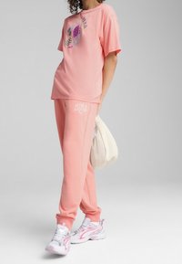 Rosa kortärmad t-shirt med grafisk design, matchad med joggers och vita sneakers med rosa detaljer, samt en lätt väska.