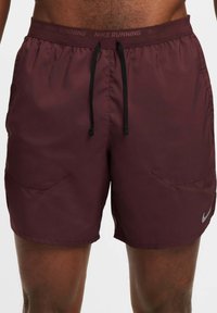 Bordeaux Nike juoksushortsit mustalla narulla, elastisella vyötäröllä ja sivutaskuilla. Alareunassa on pieni hopeinen logo.