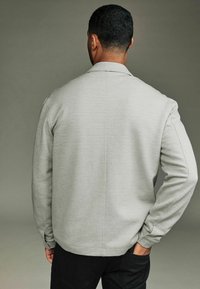 Light gray zip-up sweatshirt with a collar and textured fabric, featuring side pockets and ribbed cuffs. Back view with relaxed fit.