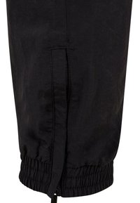 Schwarze, zulaufende Hose mit elastischem Bund und Reißverschlussdetail am Saum. Hergestellt aus einem strukturierten Stoff mit glatter Oberfläche.