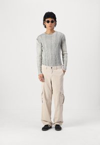 Szary prążkowany longsleeve, beżowe spodnie cargo z kordurowej tkaniny z bocznymi kieszeniami i czarne buty. Uzupełnione okrągłymi okularami przeciwsłonecznymi.