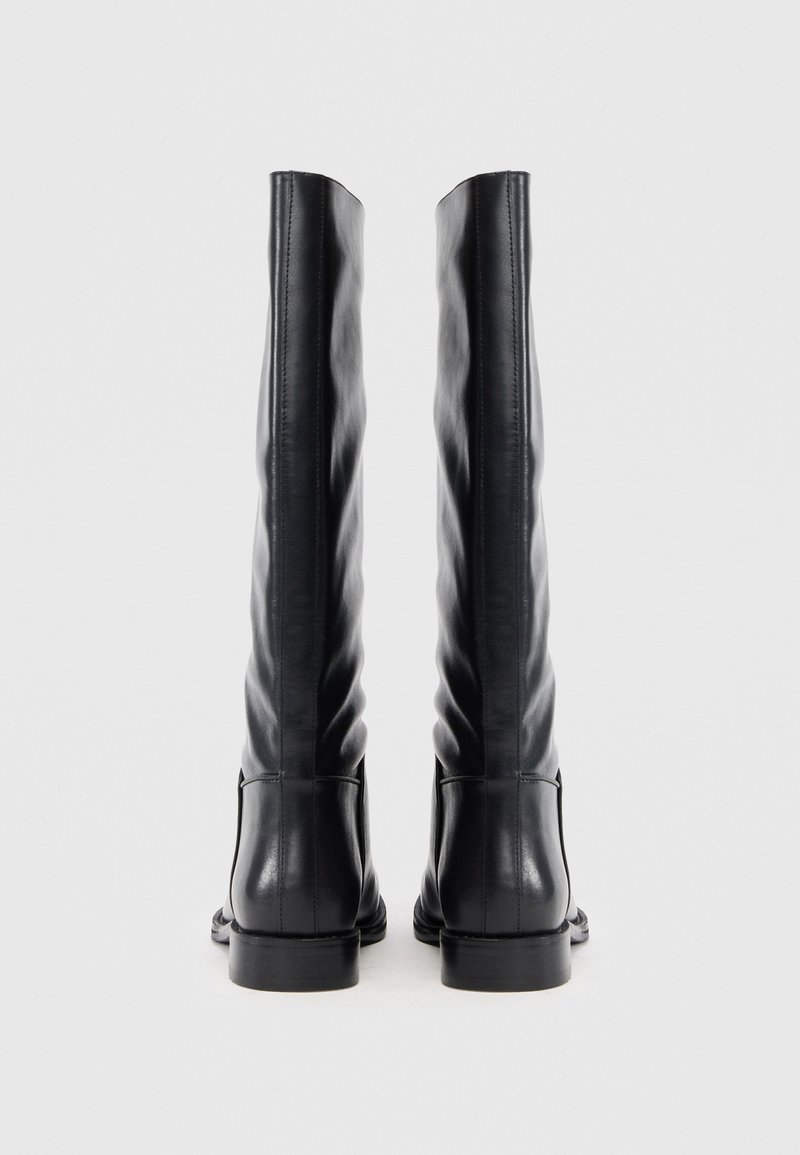 Schwarze Lederstiefel bis zum Knie mit einer eleganten, glatten Textur und dezenten vertikalen Falten. Flache Sohlen und minimales Hardware-Detail.