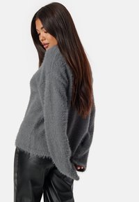 Maglione grigio e morbido con una vestibilità rilassata, maniche larghe e una finitura testurizzata, abbinato a pantaloni in finta pelle nera.