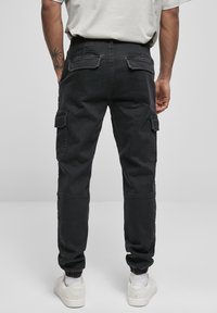 Black cargo pants with back pockets, elastic cuffs, and side pockets. Fabric has a smooth texture. Worn with white sneakers.