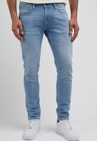 Jasnoniebieskie dżinsy o slim fit, z pięcioma kieszeniami i delikatnym wyblaknięciem. W połączeniu z białymi trampkami.