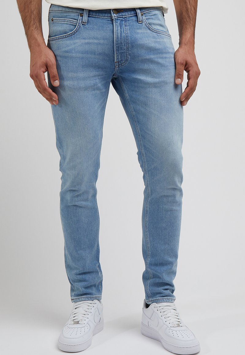 Jasnoniebieskie dżinsy o slim fit, z pięcioma kieszeniami i delikatnym wyblaknięciem. W połączeniu z białymi trampkami.