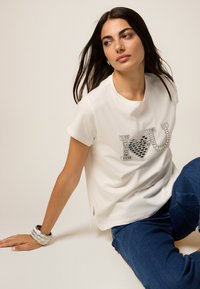Camiseta blanca de manga corta con "Te ♥ Amo" en embellishments plateados. Combinada con jeans azul oscuro. Tela suave, corte relajado.