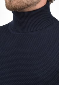 Marineblauwe coltrui met een gestructureerd honingraatpatroon en ribbelkraag. De stof lijkt glad en sluit mooi aan rond de nek.