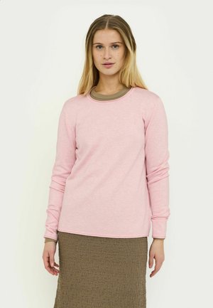 Langärmliges pinkfarbenes Oberteil mit rundem Ausschnitt, gefertigt aus weichem Stoff. Getragen über einem braunen, strukturierten Rock, hat es eine lockere Passform und sichtbare Nähte.