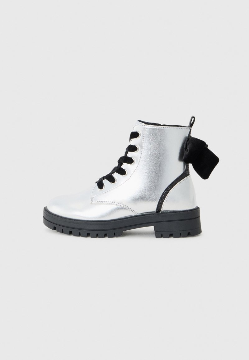 Stivaletto metallico d'argento con lacci neri, suola in gomma e un contrastante tallone nero. Presenta una texture liscia e un design robusto.