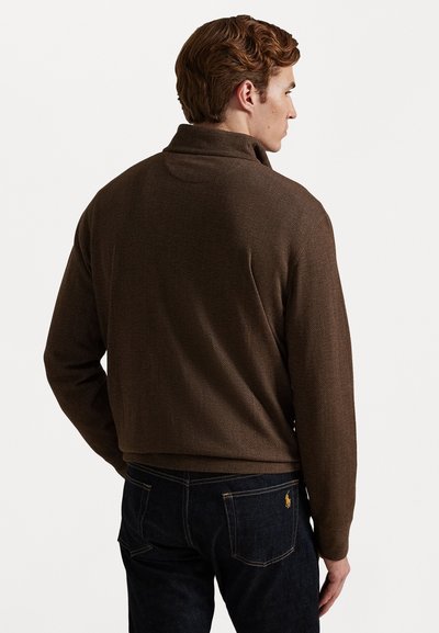 Καφέ πουλόβερ με σχέδιο ψαροκόκαλο και ψηλό γιακά, υφή υφάσματος και χαλαρή εφαρμογή, συνδυασμένο με σκούρα τζιν παντελόνια που έχουν λογότυπο στην πίσω τσέπη.