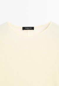 Beżowa koszulka z okrągłym dekoltem z czarną metką Massimo Dutti wszytą wewnątrz kołnierza.