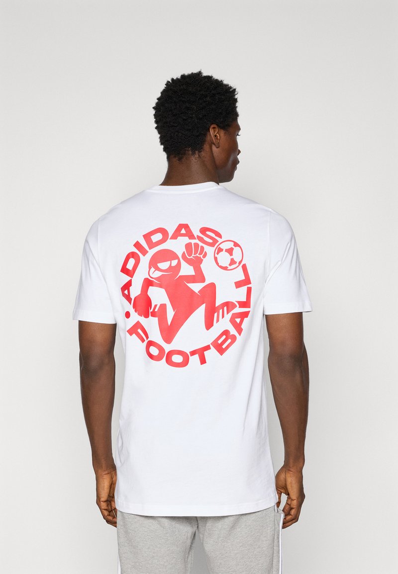 White cotton t-shirt featuring a large red graphic of a cartoon figure playing football, with "ADIDAS FOOTBALL" text surrounding the design.
