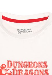 Bílá tričko s červeným límečkem, na přední straně s velkým červeným grafickým označením "Dungeons & Dragons" a černým logem draka.