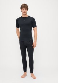 Ensemble de sport noir comprenant un haut à manches courtes avec un col rond et un pantalon long assorti, fabriqué dans un tissu lisse et extensible.