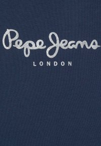 Jūras zila auduma ar metālisku sudraba tekstu, kas rakstīts fluidā skriptā "Pepe Jeans", ar "LONDON" zemāk vienkāršākā fontā.