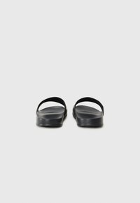 Sandales noires avec deux larges brides, semelles plates et semelle intérieure texturée. Fabriquées en matériau synthétique, elles présentent un design minimaliste.