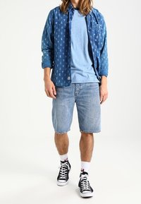 Blauwe gestreepte lange mouwen shirt over een lichtblauw t-shirt, gecombineerd met spijkerbroek shorts en zwarte sneakers met witte accenten.