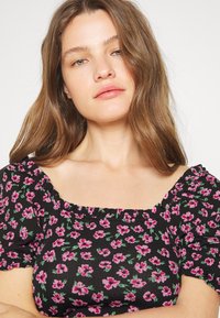 Top preto com flores, apresentando mangas curtas bufantes, decote quadrado e um padrão abrangente de flores rosas com folhas verdes.