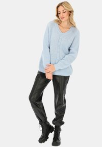 Jasnoniebieski sweter z dzianiny z dekoltem w serek i teksturowanym wzorem, zestawiony z czarnymi skórzanymi spodniami i czarnymi butami za kostkę z sznurówkami.