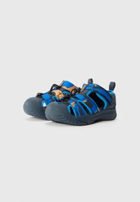 Blå och orange sportsandaler med gummisulor, justerbara remmar, övre del i nättextil och stängd tådesign för extra skydd.