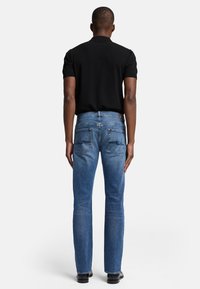 Jean en denim bleu indigo à coupe droite, avec des poches arrière ornées de coutures apparentes, porté avec un haut noir à manches courtes.