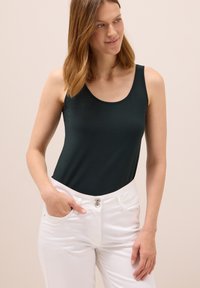 Grön ärmlös topp i mjukt tyg, kombinerad med vita högmidjade byxor. Toppen har en rund halsringning och en figurnära siluett.