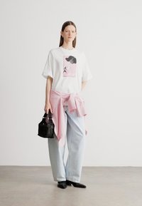 Valge ülisuur T-särk roosa graafikaga, helesinised laia säärega teksad, roosad triibulised seelik ja väike must käekott.