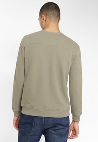Khaki sweter z teksturalnym wykończeniem, okrągłym dekoltem i ściągaczami. W połączeniu z ciemnoniebieskimi dżinsami, minimalne detale w szwie.