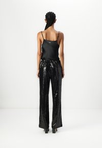 Svart satin cami med tynne stropper, kombinert med høy midje, funksjonell, svart bukser i paljetter. Buksene har en rett ben-design og en skinnende tekstur.
