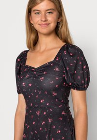 Vestido preto floral com mangas curtas bufantes, apresenta um decote quadrado e pequenas flores cor-de-rosa. Feito de um tecido suave e elástico.