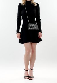 Vestido largo negro de manga larga con falda acampanada, acompañado de un pequeño bolso a cuadros y sandalias negras de tacón alto.