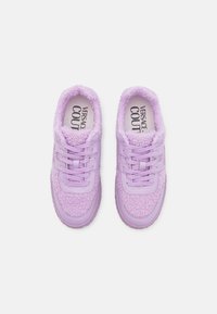 Lila sneakers med texturerad tygöverdel och slät gummisula. Har rund tå, snörning och mjukt foder. Varumärket är tryckt inuti.