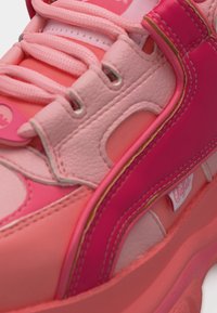 Κοντινό πλάνο ροζ και κοραλλί αθλητικού παπουτσιού με παχιά σόλα, επενδύσεις από δέρμα, κορδόνια και ορατή ετικέτα μάρκας στο πλάι.