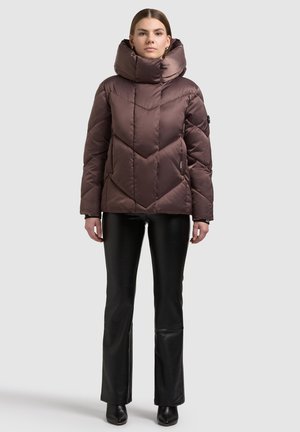 Ruskea untuvatakki, jossa korkea kaulus ja kalanruotokuvioinen tikkaus. Pehmeä, kiiltävä kangas; yhdistetty mustiin, istuviin housuihin ja nilkkureihin.