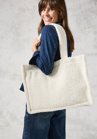 Witte fluffy totebag van textuurstof, met brede, zachte hengsels. De tas is rechthoekig met een naadloze vormgeving.