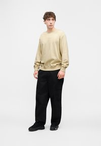 Μπεζ φούτερ με ριμπ μανσέτες και τελείωμα, φορεμένο με μαύρο cargo παντελόνι με πλαϊνές τσέπες. Το σύνολο ολοκληρώνουν αθλητικά παπούτσια.