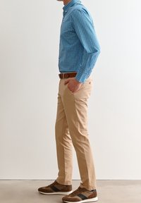 Camicia azzurra a quadretti con bottoni, chinos beige e scarpe da ginnastica marroni con strisce scure. Vestibilità slim e design casual.