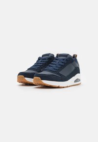 Navy blue sneakers with a combination of suede and leather, white midsole, and gum rubber outsole, featuring round laces and padded collar.