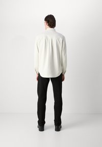Hvit langermet skjorte med rund kant, kombinert med svarte bukser. Skjorten har en glatt tekstur og en klassisk krageutforming.