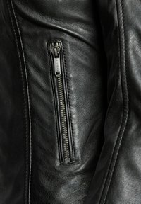 Black leather jacket section featuring a zipped pocket with a silver zipper. Texture appears smooth with seam details along the body.